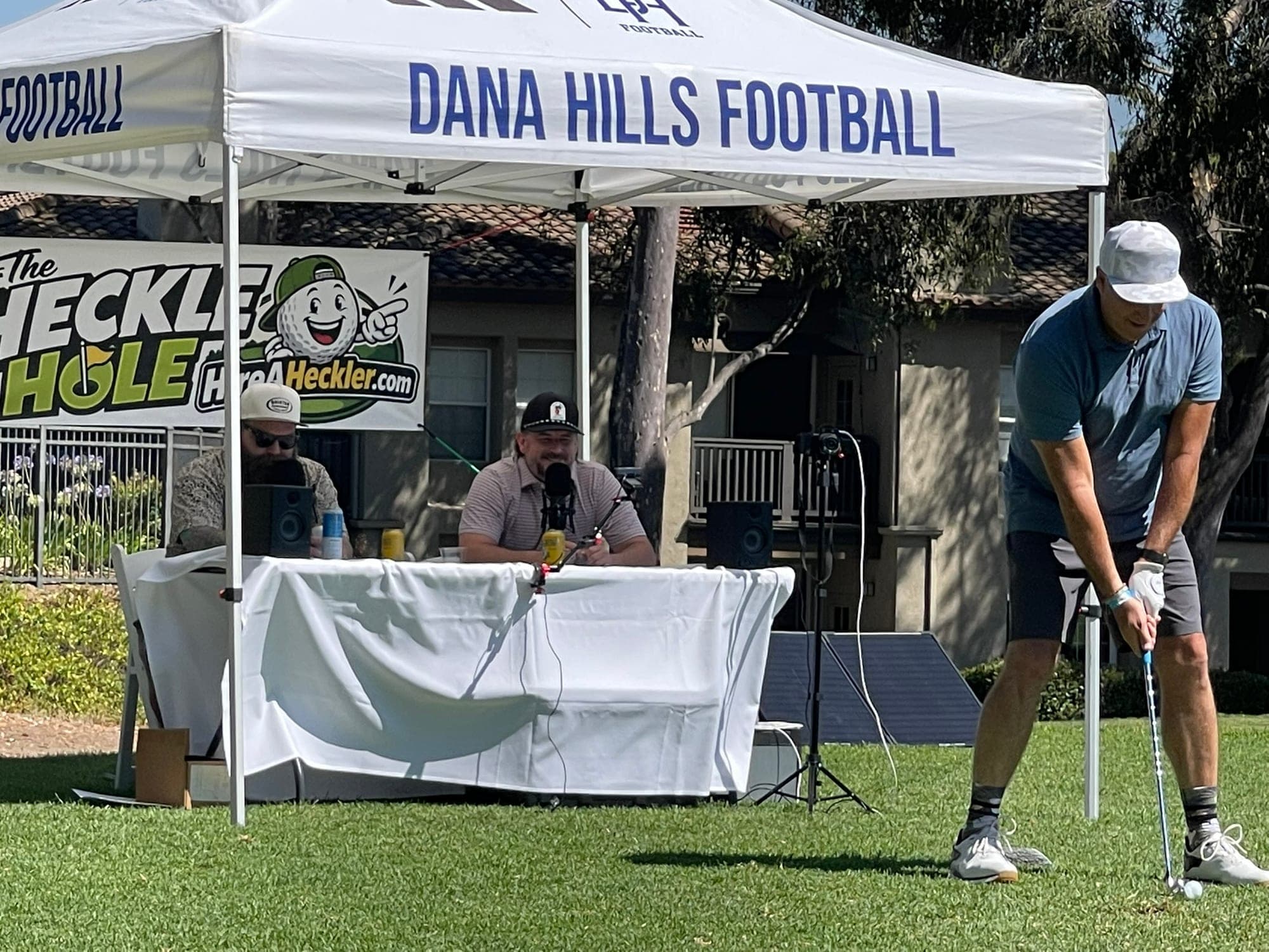 Golfer preparing to hit while Hire A Heckler comedians roast him from the tee box