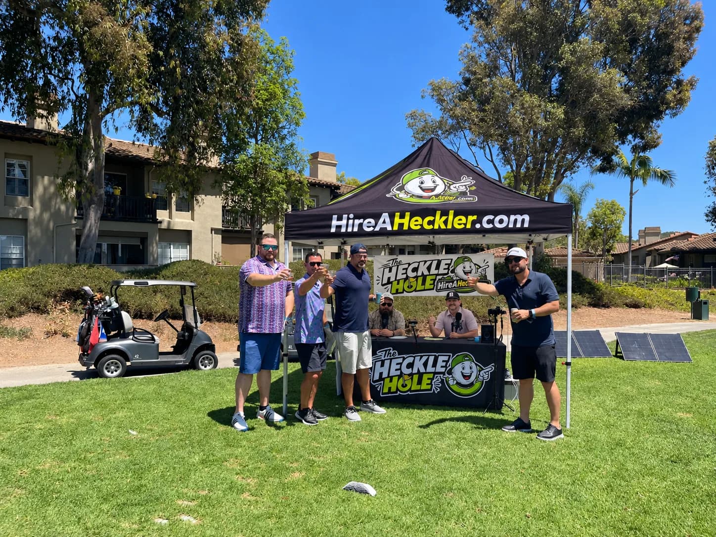 Golfers toast in front of The Heckle Hole Hire A Heckler booth on the course
